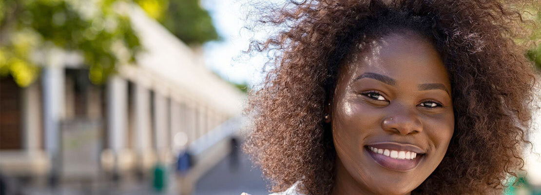 A young african american woman stands outdoors and smiles for a portrait.