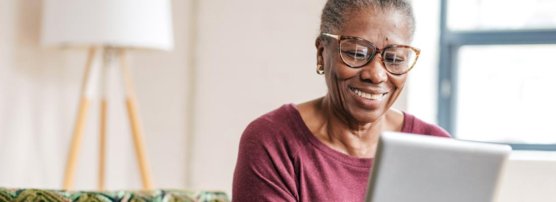 A woman sits on a sofa in her home and looks at an ipad.