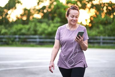 A woman walks for exercise while listening to music on a small hand-held device.