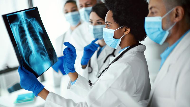 一组医生讨论一个案例而看一个x光胶片。医务人员的防护工作服分析患者x射线图像。