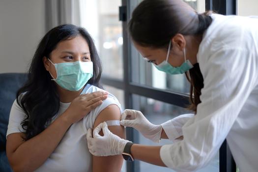 A doctor applies a band-aid to the arm of a patient after receiving a vaccine shot.