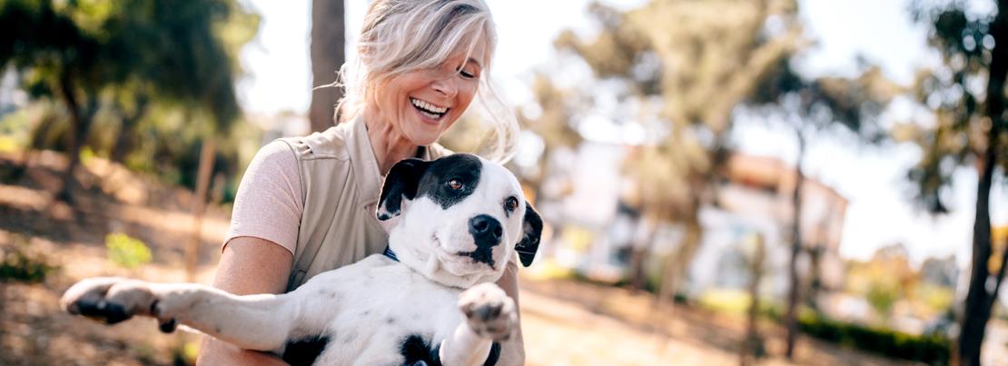 A senior woman holds her dog while enjoying a walk in the woods.