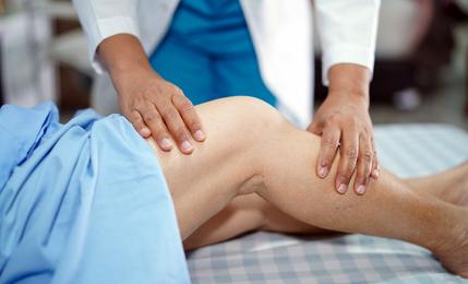A physical therapist maneuvers a patient's knee during a physical therapy session.
