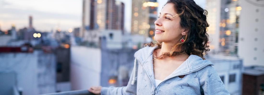 Shot of a young woman standing on the rooftop of a city building and looking away