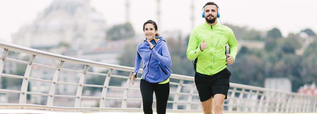 Couple running together outdoors over a bridge.
