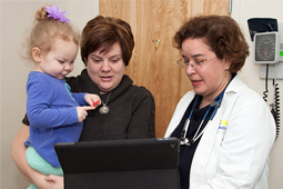 A mother, holding her young child, talks with an MMG doctor during an office visit.