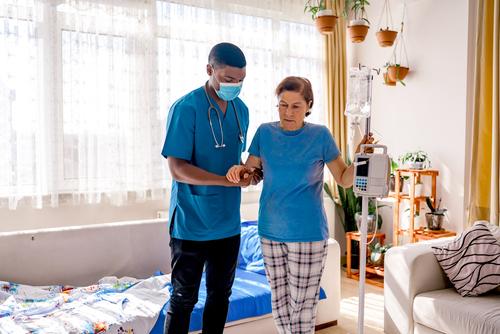 A nurse helps a senior woman walk during a home healthcare visit.