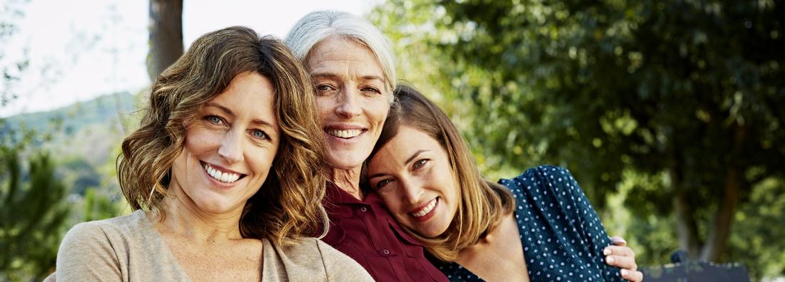 Portrait of happy mother sitting with daughters on park bench