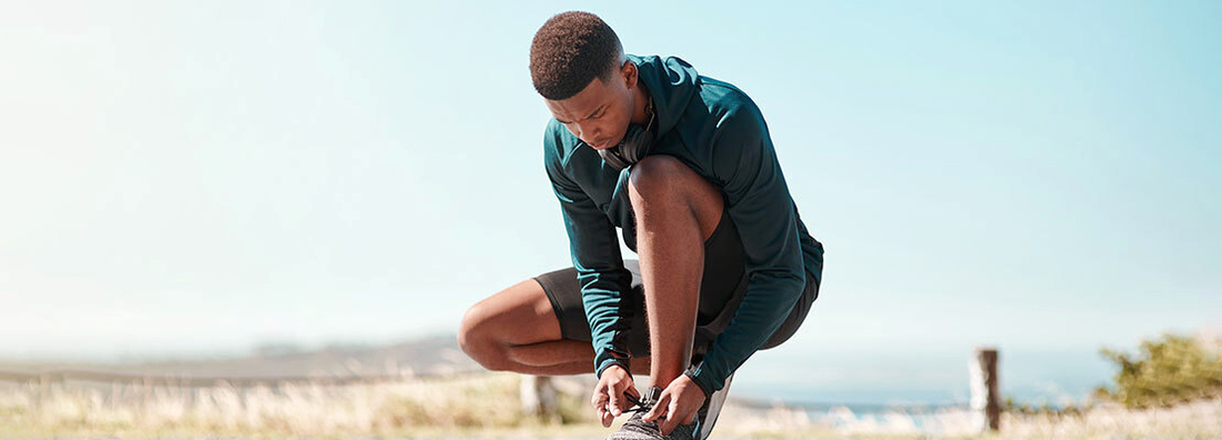 A young athletic man crouches down and ties his shoelaces before going for a run outdoors