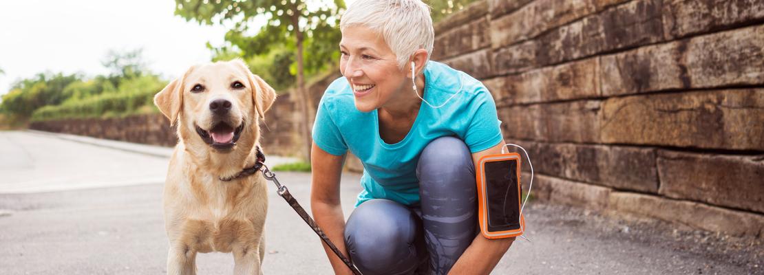 A senior woman crouches down close to her dog while out for a run.