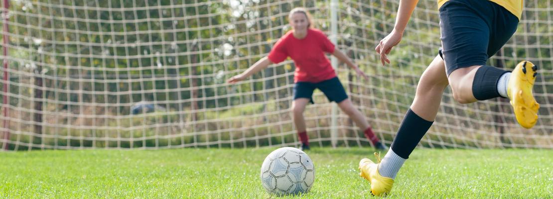 Close up of an athlete kicking a soccer ball toward the goalie.