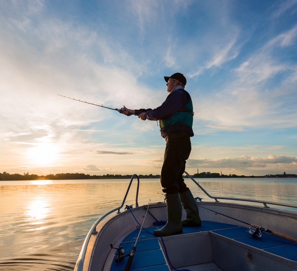 A man fishes off of a boat on a large body of water at sunset.