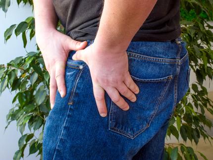 Close up photo of a man clutching his hip in pain.
