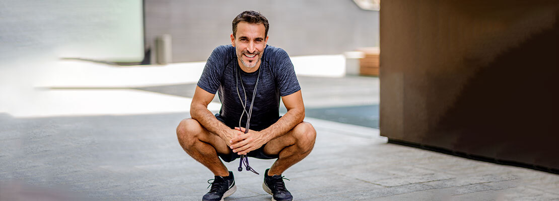 A young athletic man crouches down between jump rope sets during a workout.