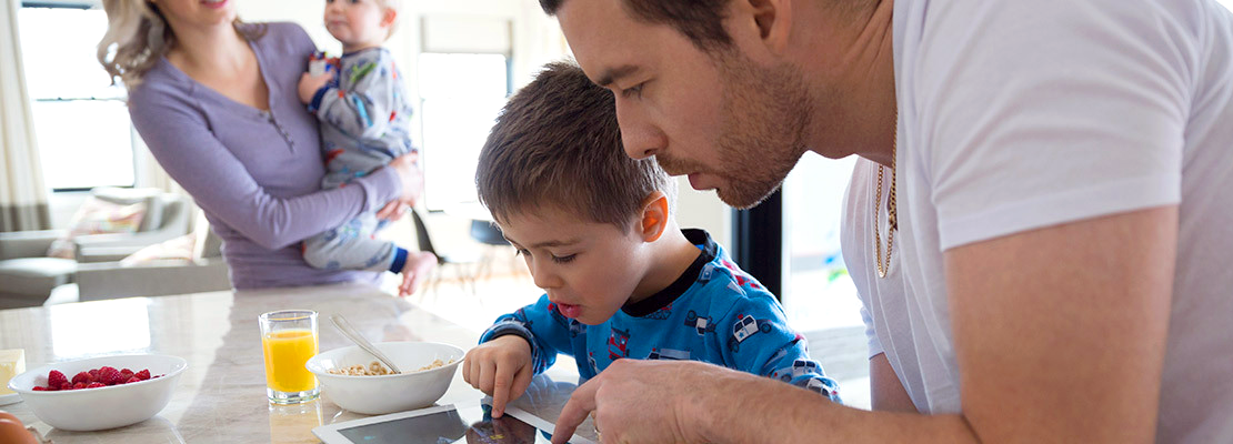 A father and son look at an ipad during family breakfast in the kitchen.