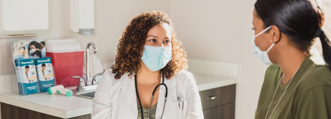 A female doctor talks with a female patient in a clinical setting.