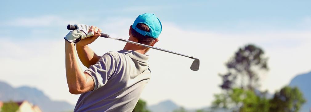 A man hits a golf ball on a golf course in a warm sunny location.