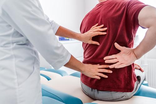 A close up photo of a doctor placing hands on a patient's back during an examination.