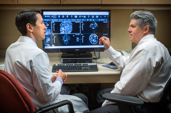Doctors Chia and Aulisi sit and talk in front of a computer monitor which shows scans a head and neck. 