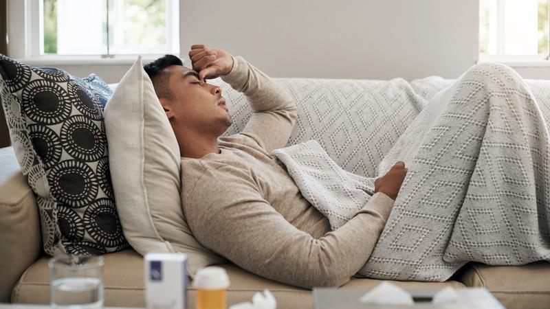 A young man lays on his couch at home feeling sick.