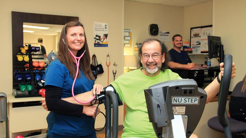A MedStar Health rehabilitation nurse helps a patient while he rides a recumbent bike in a rehabilitation gym.