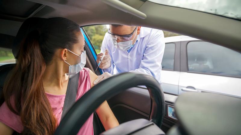 A nurse administers a vaccination shot to a patient at a drive-thru vaccination event.