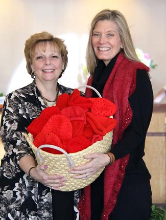 Ellen Lewis and Mary Cheseldine hold a basket of red newborn hats that were donated to MedStar St Mary's Hospital.
