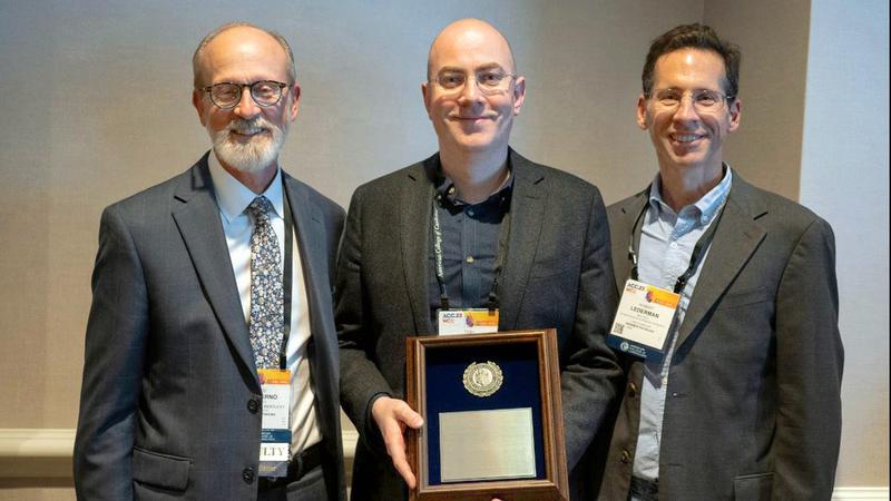 Toby Rogers holds the Young Author Achievement Award, while a representative from the American College of Cardiology stand on either side of him.