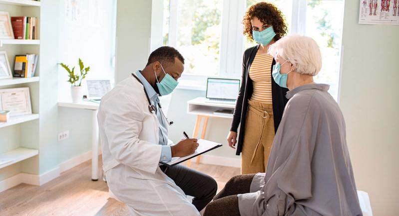 A doctor writes a prescription for an elderly patient accompanied by a younger female family member.