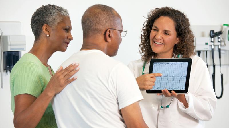 A doctor shows EKG results to a patient and spouse in a clinical setting. 