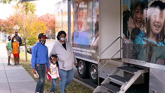 A family walks into the Mobile Health Clinic truck parked on a neighborhood street.