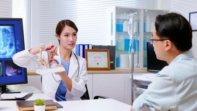 A doctor discusses with a patient in an office setting using an anatomical model of the colon.