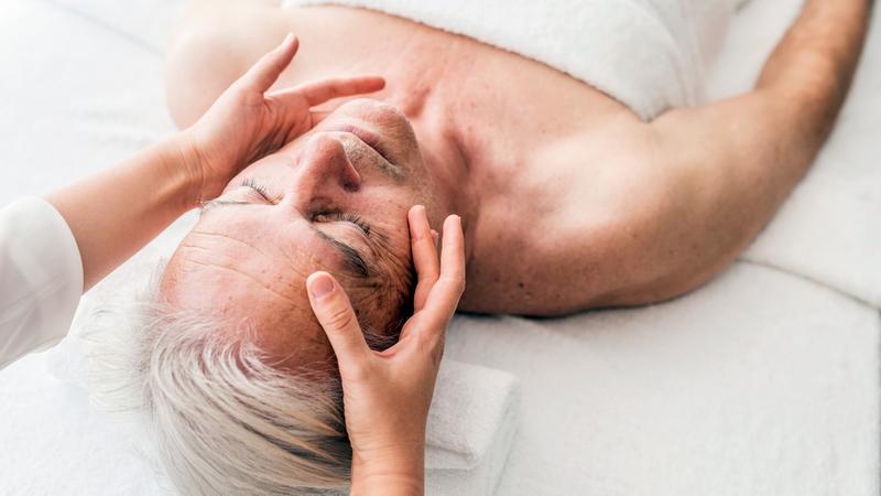 Close up photo of a massage therapist's hands on an elderly man's face.