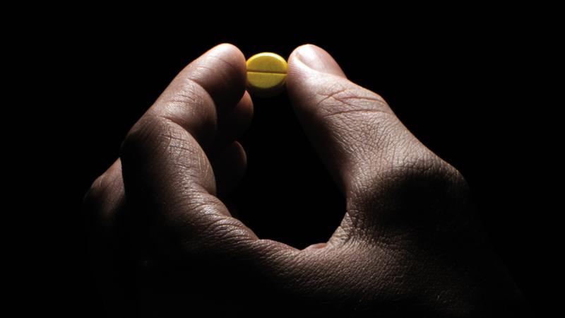 Close up photo of a hand holding a single pill, with dramatic lighting.