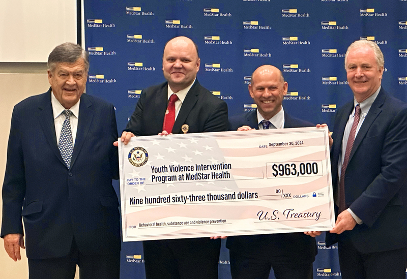 Maryland Representative Dutch Ruppersberger, Dr. Cornleiu Sanda, Stuart Levine and Senator Chris Van Hollen hold a large donation check during a presentation.