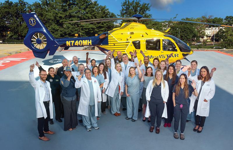 Members of the Burn Center team stand and pose for a photo in front of the MedStar helicopter on the hospital helipad
