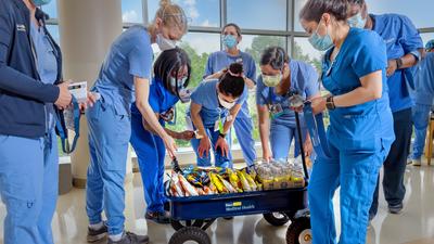 一群身穿蓝色工作服的医疗专业人员，从“健康马车”上挑选物品，以促进MedStar健康中心的医护人员健康。