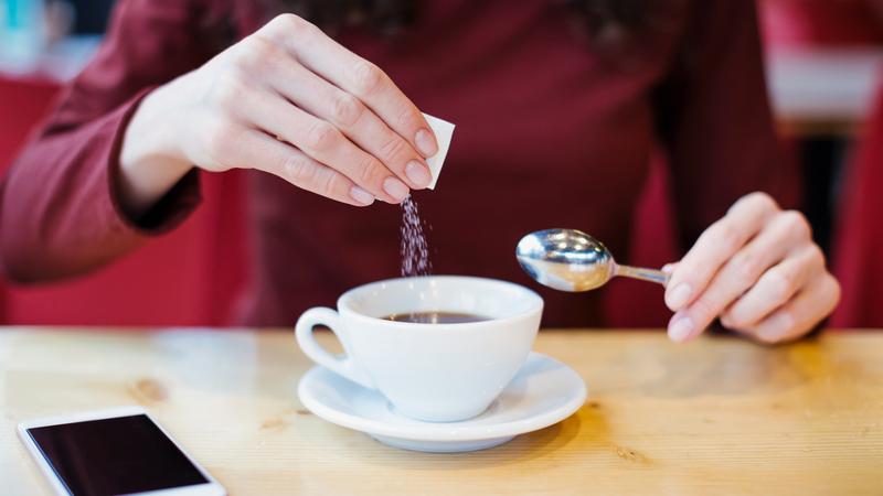 近距离的照片,一个女人将甜味剂放入一杯咖啡。