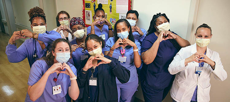 A group of nurses at MedStar Southern Maryland Hospital Center stand together for a group photo and hold their hands in a heart shape. Everyone pictured is wearing a mask.