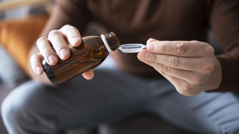 Close up photo of a man pouring cough syrup into a spoon.