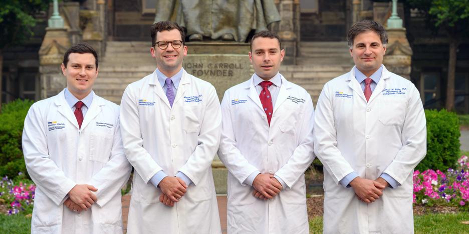 Four chief residents wearing white lab coats from the Orthopedic Residency Program in Washington DC stand together outdoors for a group photo.