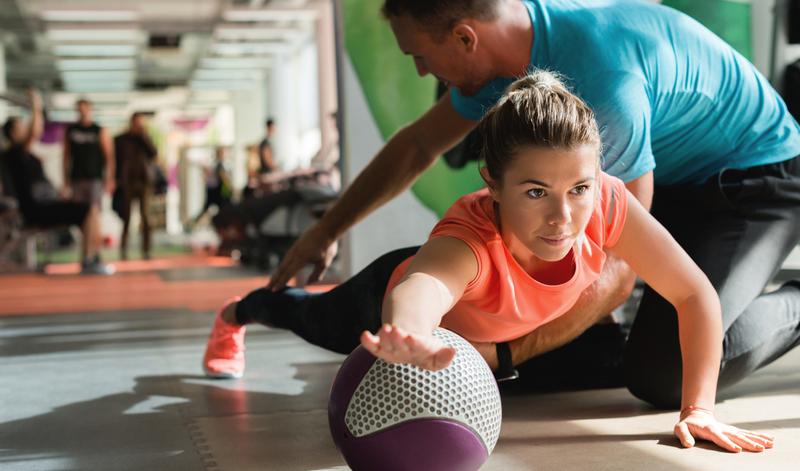 A sports medicine professional helps a female athlete with strength training.