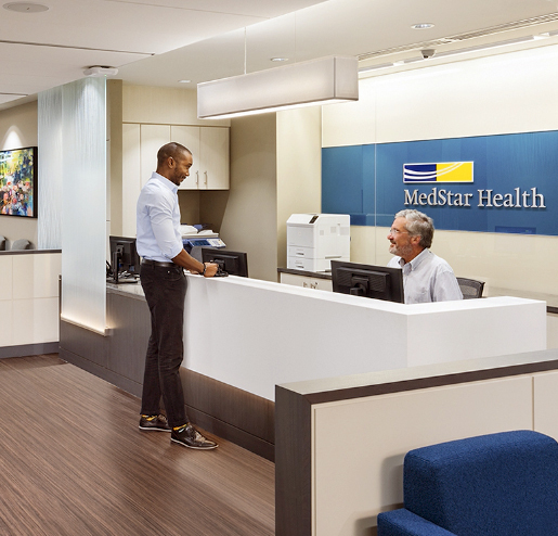 A male patient chats with a male receptionist at the front desk of a MedStar office location.