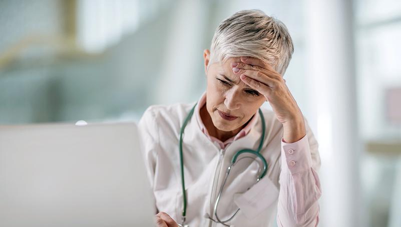 A doctor looks at a laptop comptuer while resting her head on her hand.