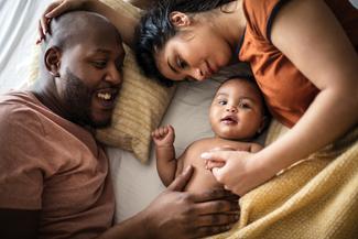 A newborn baby lays with parents on a bed.