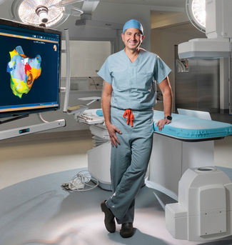 Dr Zayd Eldadah, wearing green scrubs and a blue skull cap, stands with his hands on his hips and looks at the camera in an operating room at MedStar Washington Hospital Center.