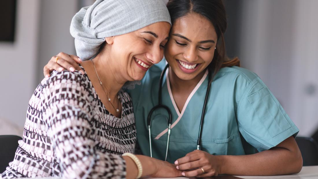 A female medical professional comforts a female patient who is wearing a head scarf.