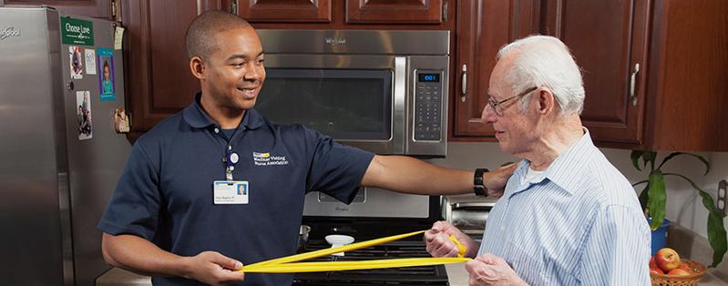 A MedStar NRH home care physical therapist helps a senior citizen patient do therapy using resistance bands in his kitchen.