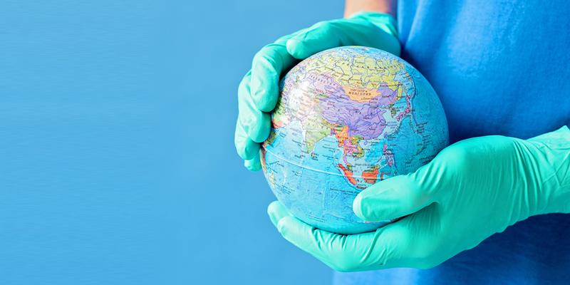 Close up photo of a person holding a small globe while wearing medical gloves.