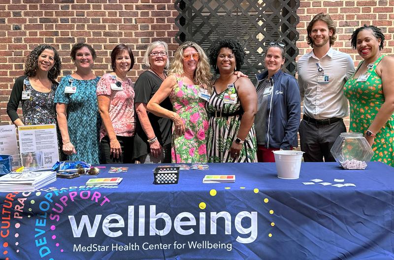 The wellbeing team from MedStar Health stands together for a group photo behind an exhibit table at an outdoor event.